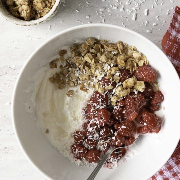 Jogurto dubenėlis su avietėmis, granola ir kokosų drožlėmis.